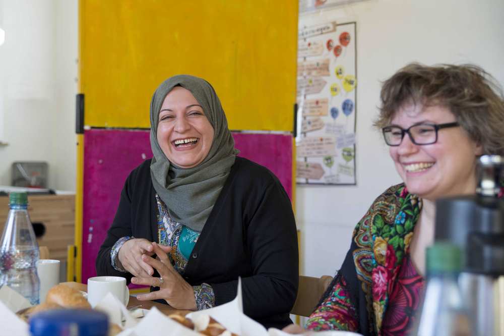 Zwei Frauen sitzen am Tisch. Sie lachen.