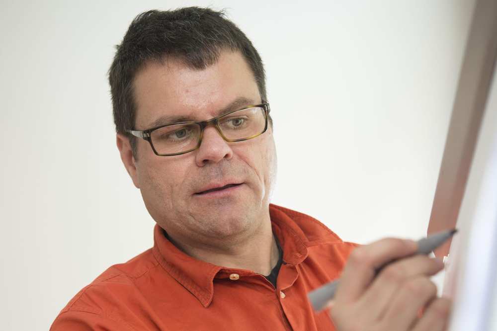 Ein Lehrer im roten Hemd schreibt an eine Tafel.