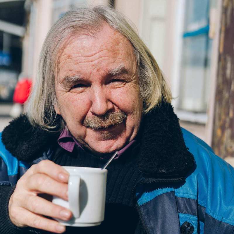 Ein älterer Mann mit Bart hält eine Kaffeetasse in der Hand.