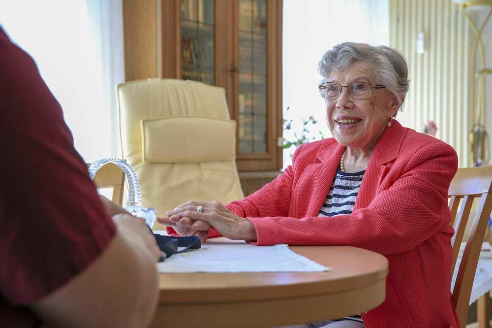 Eine Seniorin sitzt am Tisch und unterhält sich mit einem Pfleger.