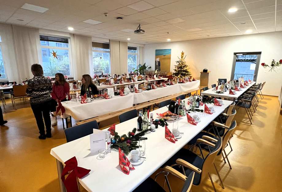 Der Saal des Christine-Kreller-Hauses ist weihnachtlich dekoriert und gedeckt. Drei Mitarbeitende sitzen am Tisch, unterhalten sich und warten auf die Gäste.