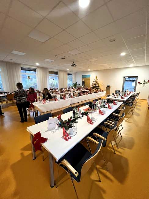 Der Saal des Christine-Kreller-Hauses ist weihnachtlich dekoriert und gedeckt. Drei Mitarbeitende sitzen am Tisch, unterhalten sich und warten auf die Gäste.