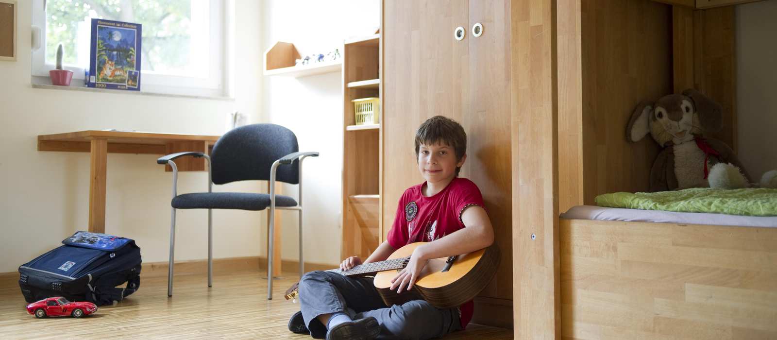 Ein Junge sitzt mit einer Gitarre auf dem Boden in seinem Zimmer.