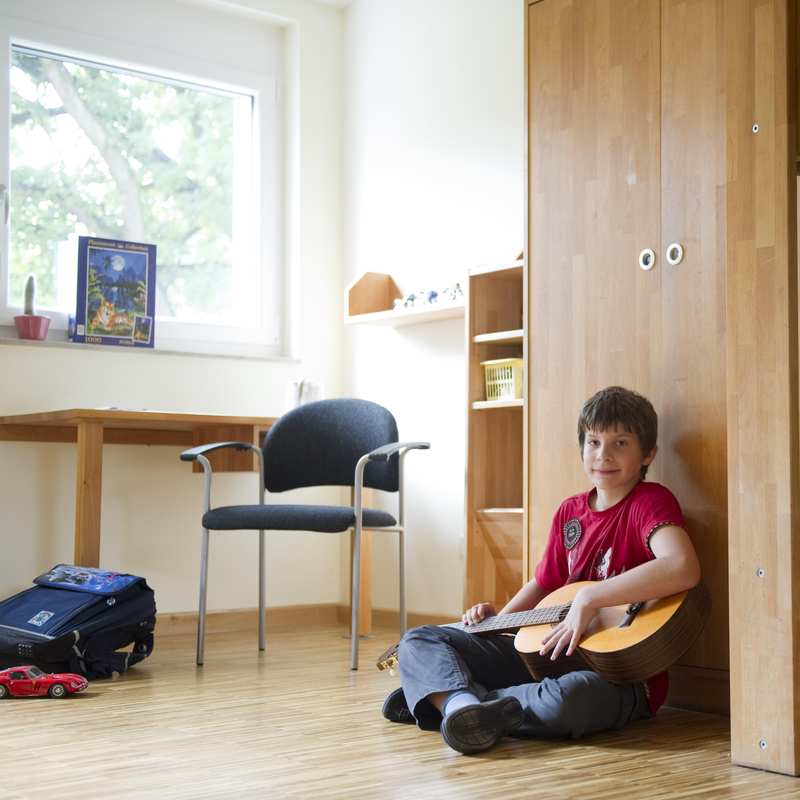 Ein Junge sitzt mit einer Gitarre auf dem Boden in seinem Zimmer.