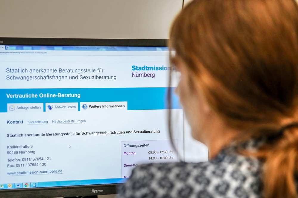 Eine Frau sitzt vor einem Computerbildschirm, auf dem die Startseite der Onlineberatung für Schwangerschafts- und Sexualfragen abgebildet ist.