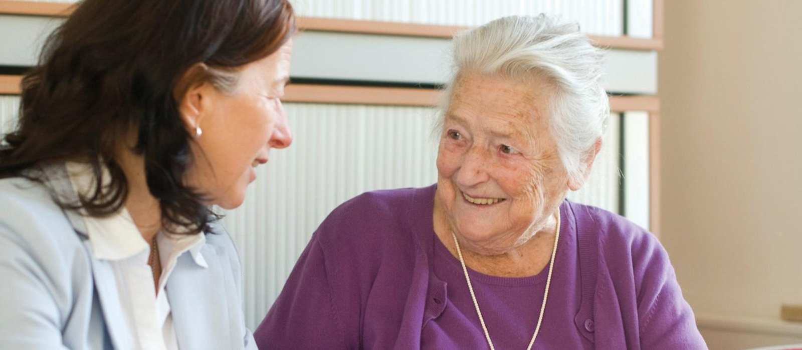 Eine Frau ist im Gespräch mit einer Seniorin.