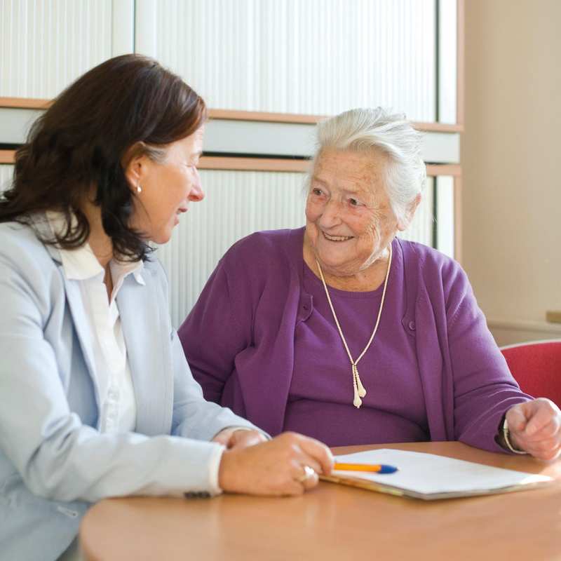 Eine Frau ist im Gespräch mit einer Seniorin.