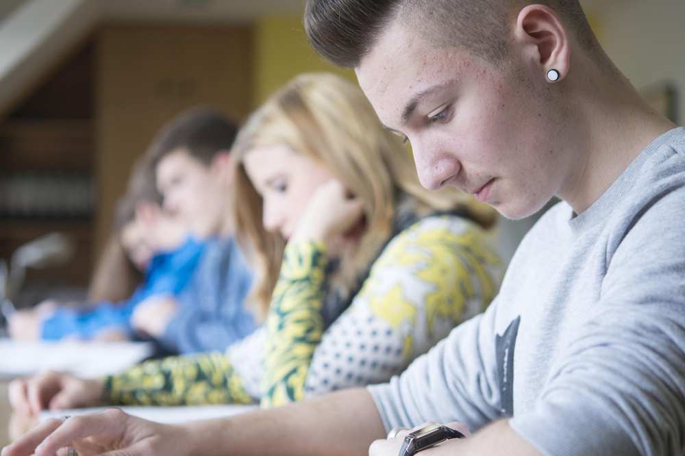 Mehrere Schülerinnen und Schüler sitzen nebeneinander an Schreibtischen.