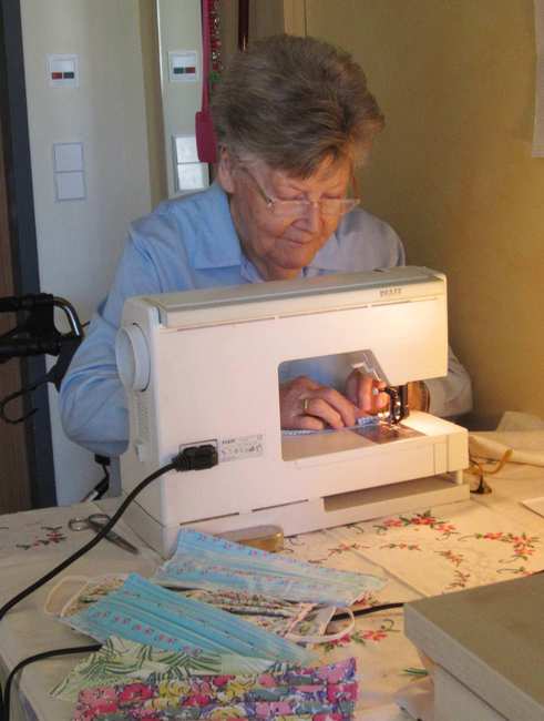 Eine alte Dame mit grauen kurzen Haaren sitzt konzentriert hinter einer Nähmaschine.