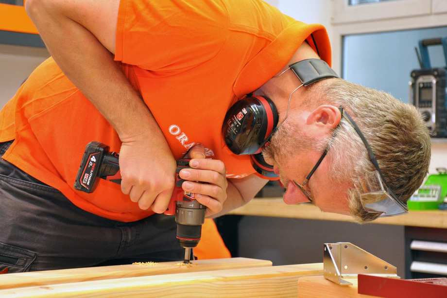 Ein Mann bohrt mit einer Bohrmaschine ein Loch in einen Holzbalken.