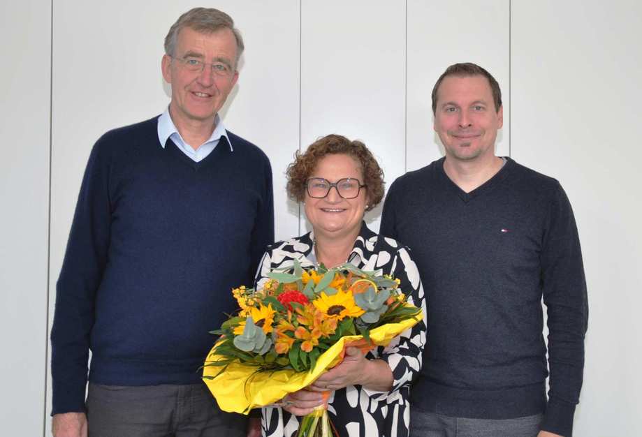 Joachim Pietzcker und Kai Stähler von der Stadtmission stehen zur Rechten und Linken von Gudrun M. Barth. Die neue Finanzvorständin hält einen Blumenstrauß in ihren Händen und lächelt.