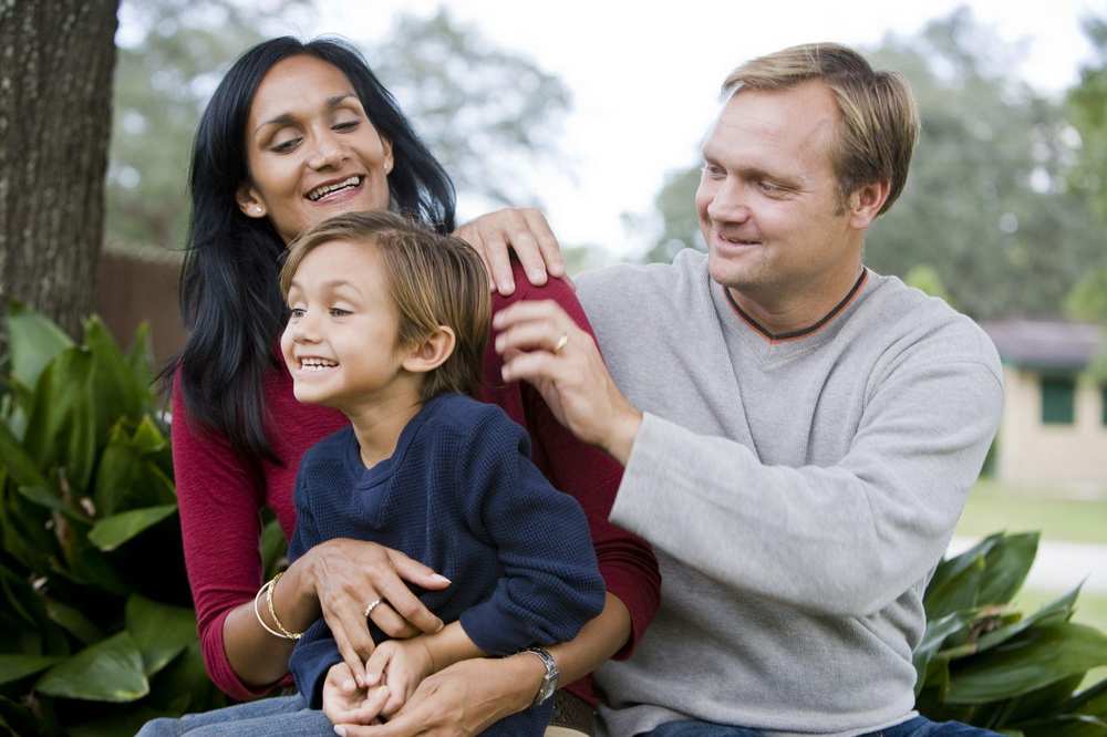 Vater, Mutter und ein kleiner Junge sitzen im Garten.