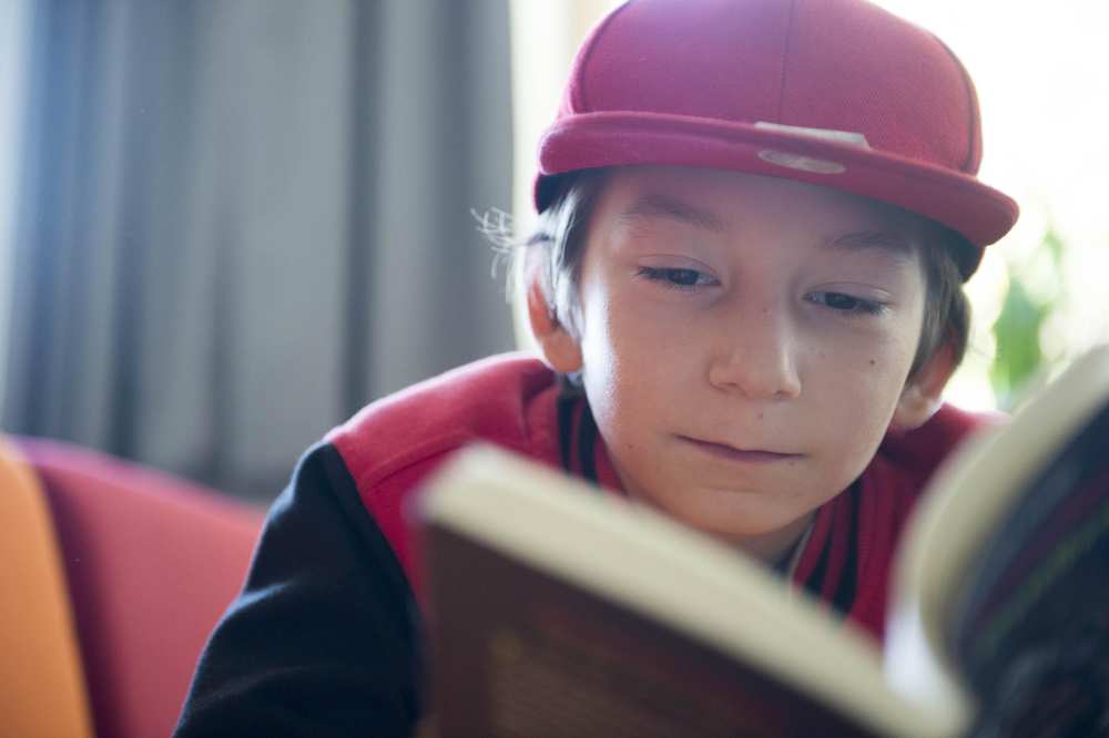 Ein Junge mit roter Kappe liest ein Buch.