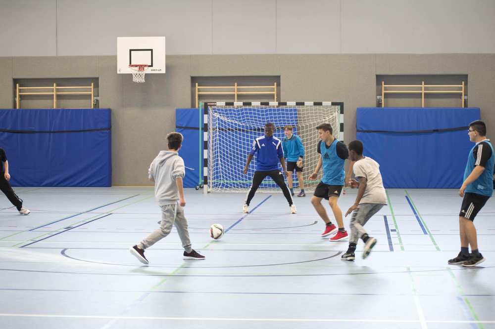 Mehrere Jungs spielen Fußball in einer Halle.