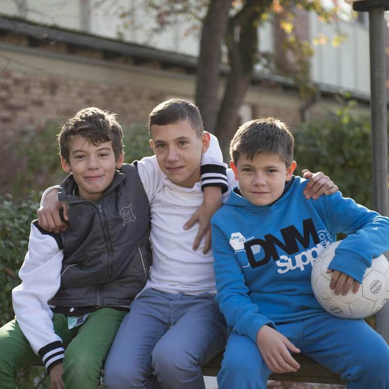 Drei Jungs mit einem weißen Fußball umarmen sich.